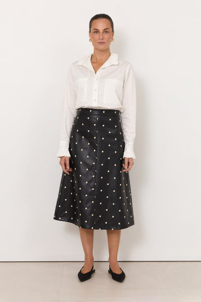 Woman wearing a white blouse and black polka dot skirt against a white background