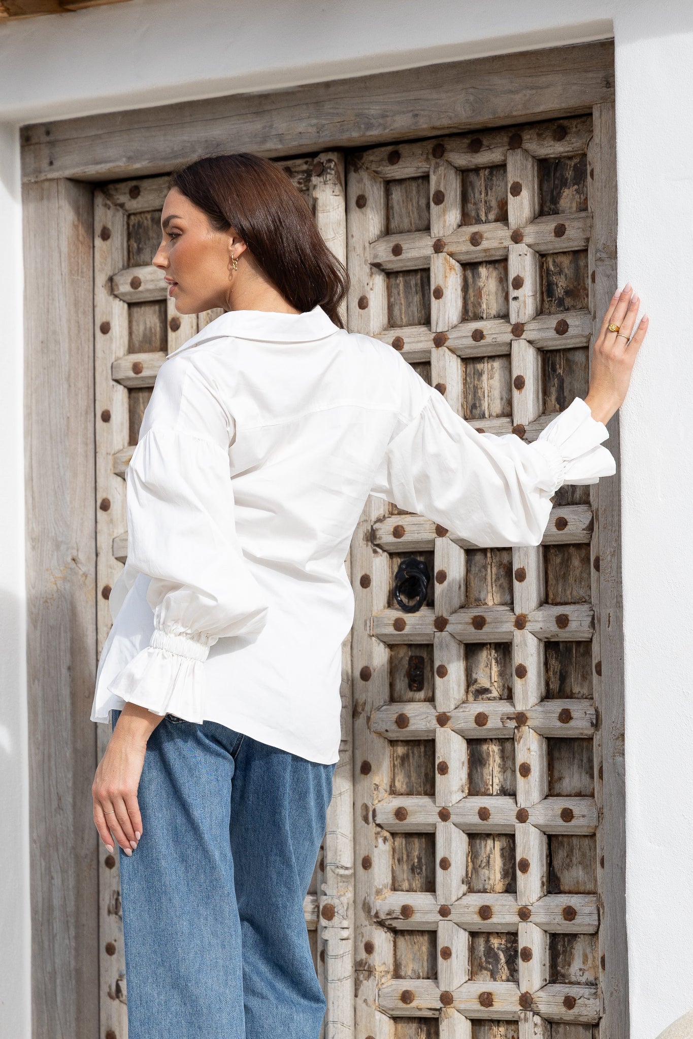 Woman in a white shirt and blue jeans standing in front of a wooden door.